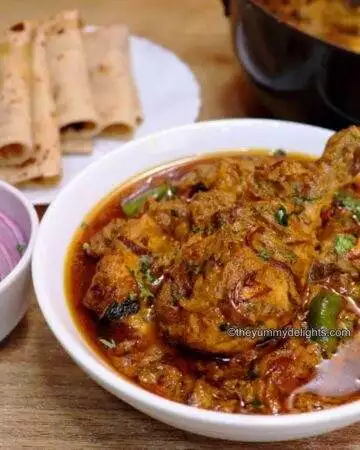 close-up of dum ka chicken. It is served with roti and onion slices and lemon wedge.