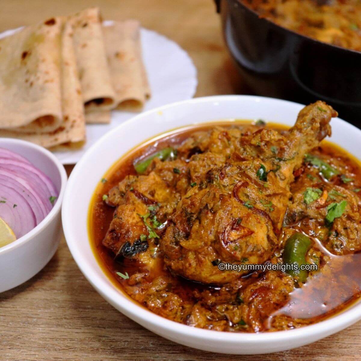 close-up of dum ka chicken. It is served with roti and onion slices and lemon wedge.