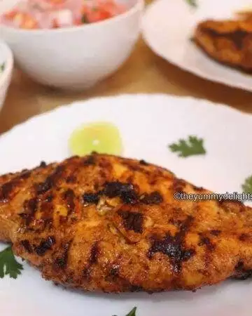 Close-up of Greek yogurt chicken marinade recipe. Greek Yogurt marinated chicken breast is placed on a white plate. Garnished with Parsley and lemon slices.