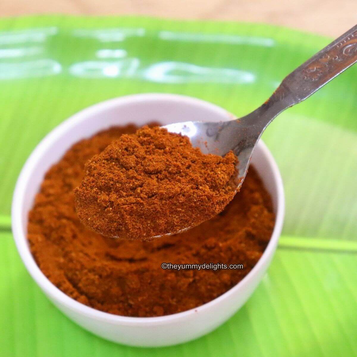 close-up of Madras curry powder in a white bowl with a spoonful of curry powder taken out of the bowl.