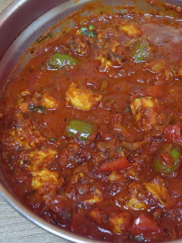 close-up of chicken Balti served in a Balti bowl. Garnished with coriander leaves. It is served with raita and salad on the side.
