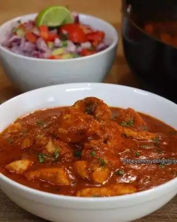 close-up of chicken chasni served in a white bowl. Along with it a bowl full of salad is served on the side.