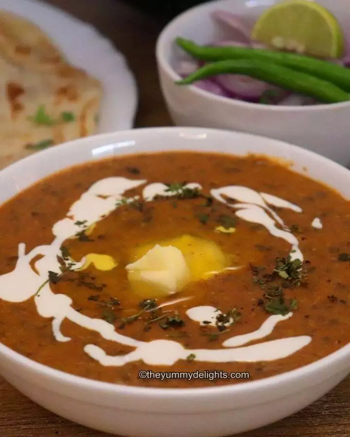 close-up of punjabi dal makhani recipe served in a white bowl with Naan and salad on the side.