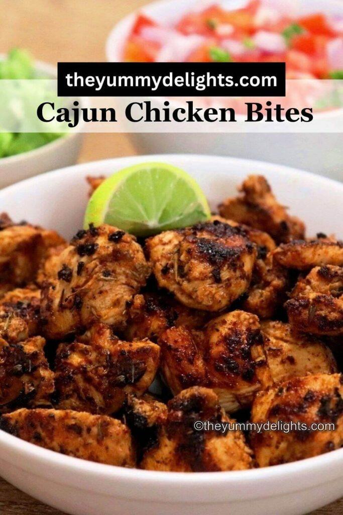 close-up of spicy cajun chicken bites served in a white bowl. A bowl of salad is served on the side. 