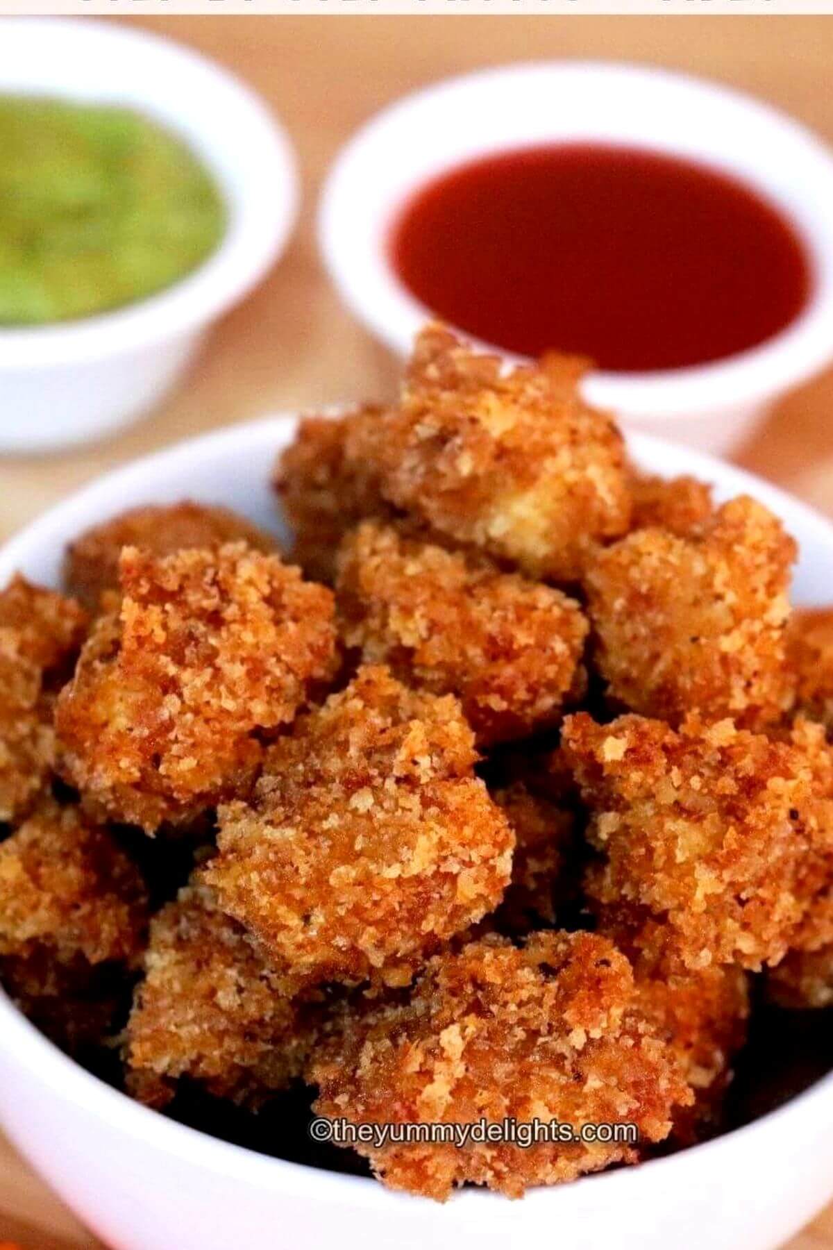 close-up of bowl full of popcorn chicken. It is served with tomato ketchup and green chutney on the side.