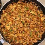 close-up of schezwan chicken fried rice recipe in a black colored pan. Garnished with spring onion greens.