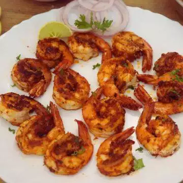 Cajun shrimp served on a white colored plate with onion rings and lemon wedges.