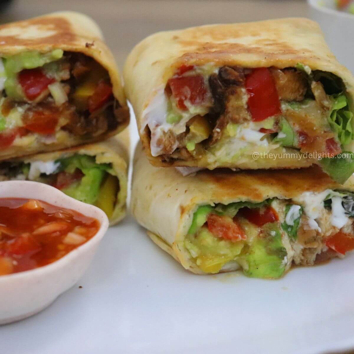 close-up of chicken fajita wrap. They are sliced and stacked on a white plate. Served with salsa dip.