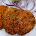 close-up of crispy king fish fry goan style served on a white plate with onion rings and lemon wedge.