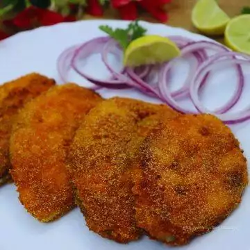 close-up of crispy king fish fry goan style served on a white plate with onion rings and lemon wedge.