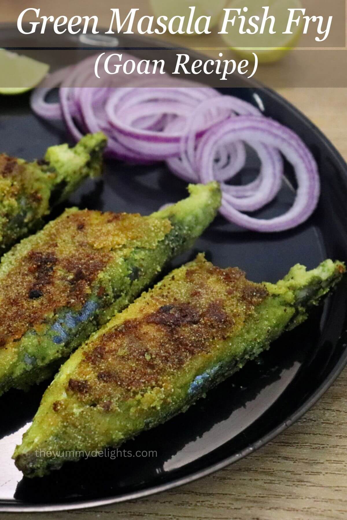 Green masala fish fry served on a black plate with onion rings and a lemon wedge.