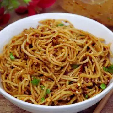 A bowl of spicy chili oil noodles topped with sesame seeds and scallions.
