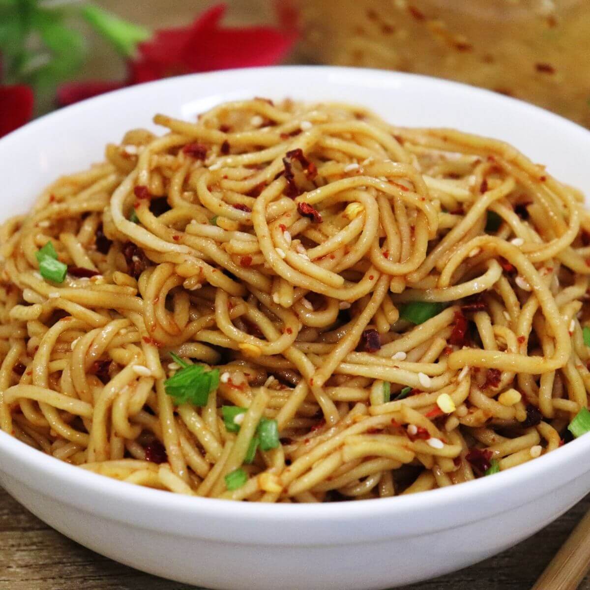 A bowl of spicy chili oil noodles topped with sesame seeds and scallions.