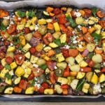 close-up of mediterranean oven roasted vegetables in a baking sheet. Garnished with Feta cheese and basil leaves.