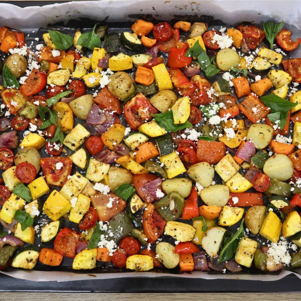 close-up of mediterranean oven roasted vegetables in a baking sheet. Garnished with Feta cheese and basil leaves.