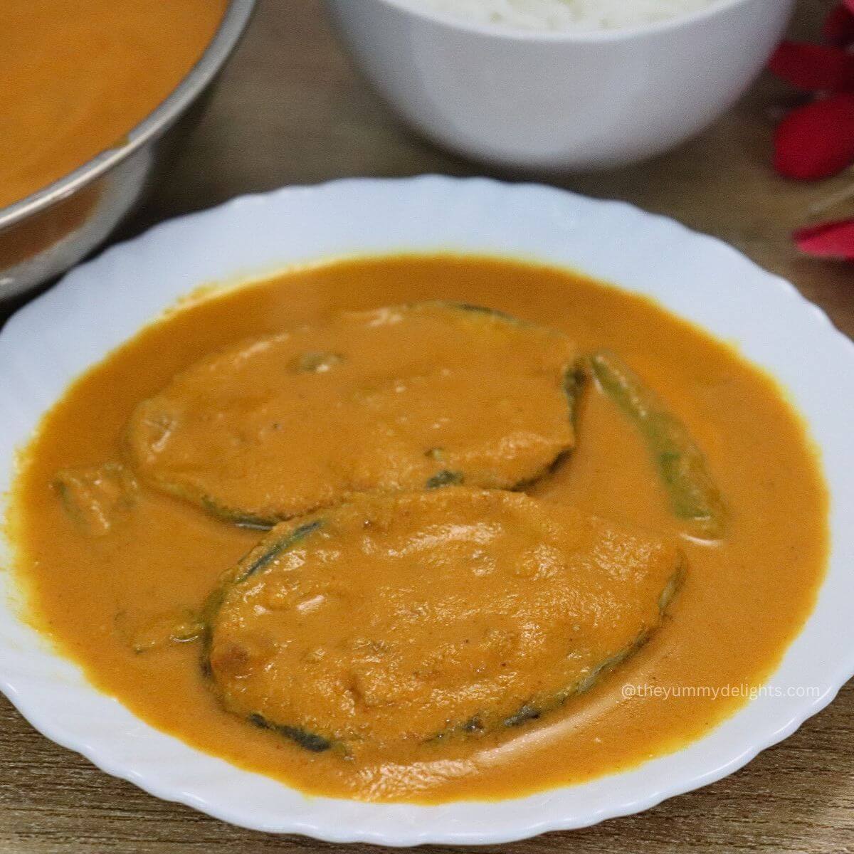 close-up of kingfish curry served on a white plate with a bowl full of rice on the side.