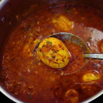 close-up of dhaba-style egg curry in a ladle, held over a rustic pot of spicy onion tomato masala and garnished with fresh coriander.