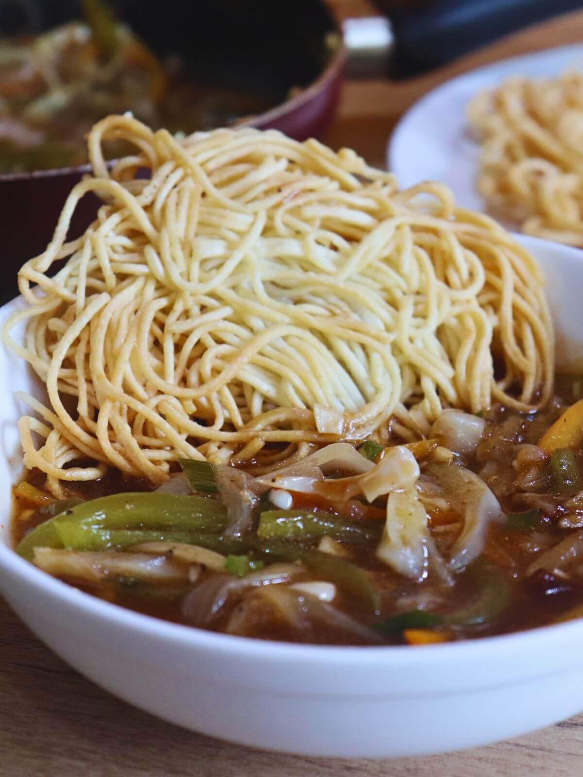 close-up of american chop suey served in white bowl. It is served with fried noodles.