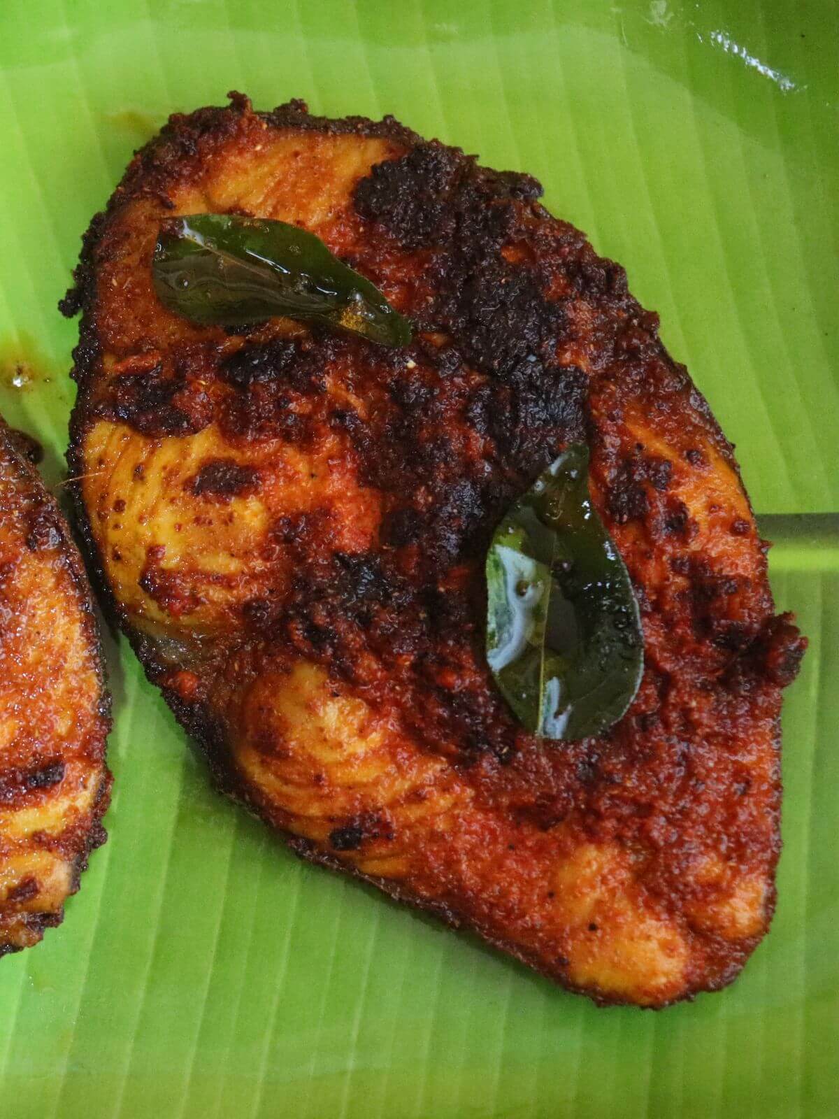 close-up of andhra fish fry. It shows one fried fish served on a green color plate, garnished with curry leaves.