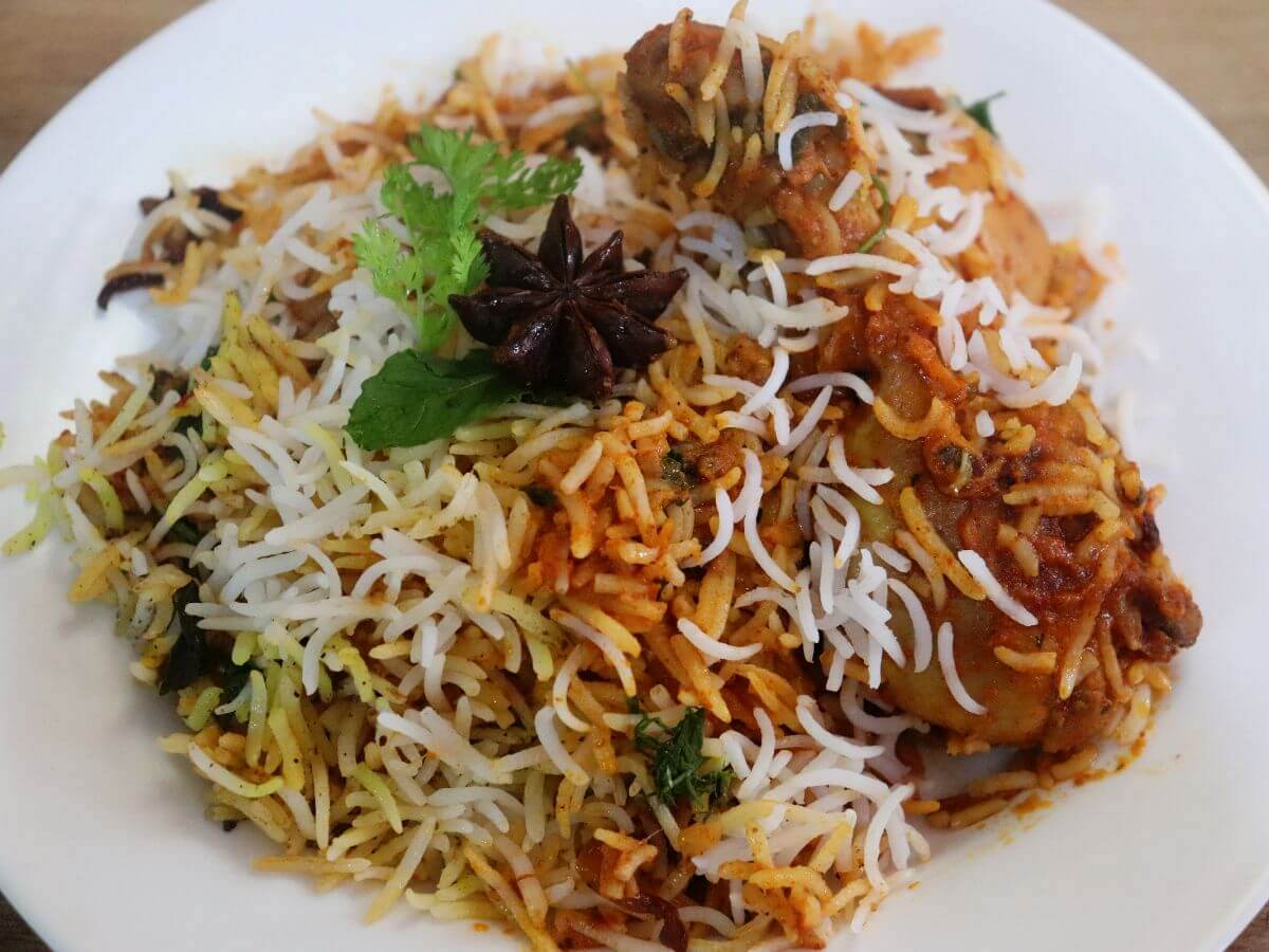 top shot of butter chicken biryani served in a plate. It is garnished with mint and coriander leaves.