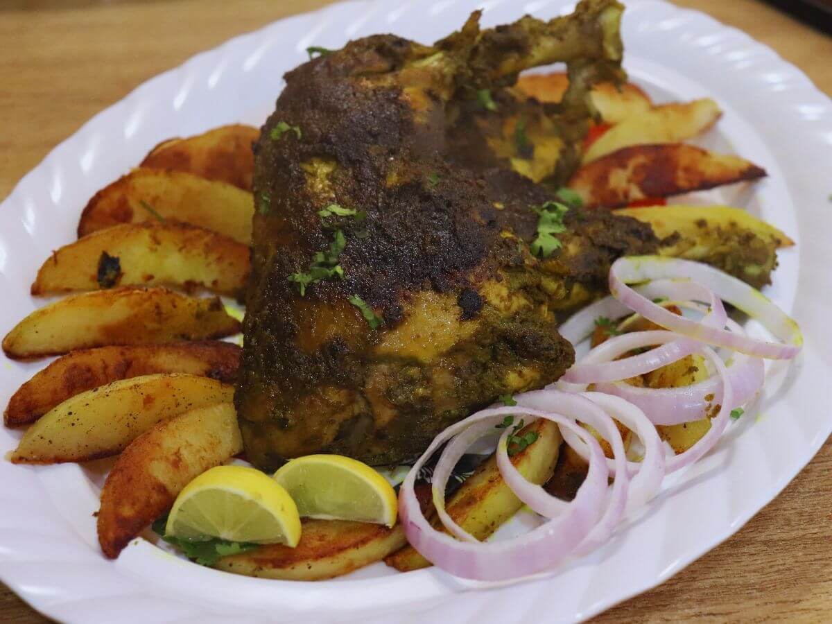 close-up of chicken cafreal served in a white colored plate with roasted potato wedges, onion rings and lemon wedges.