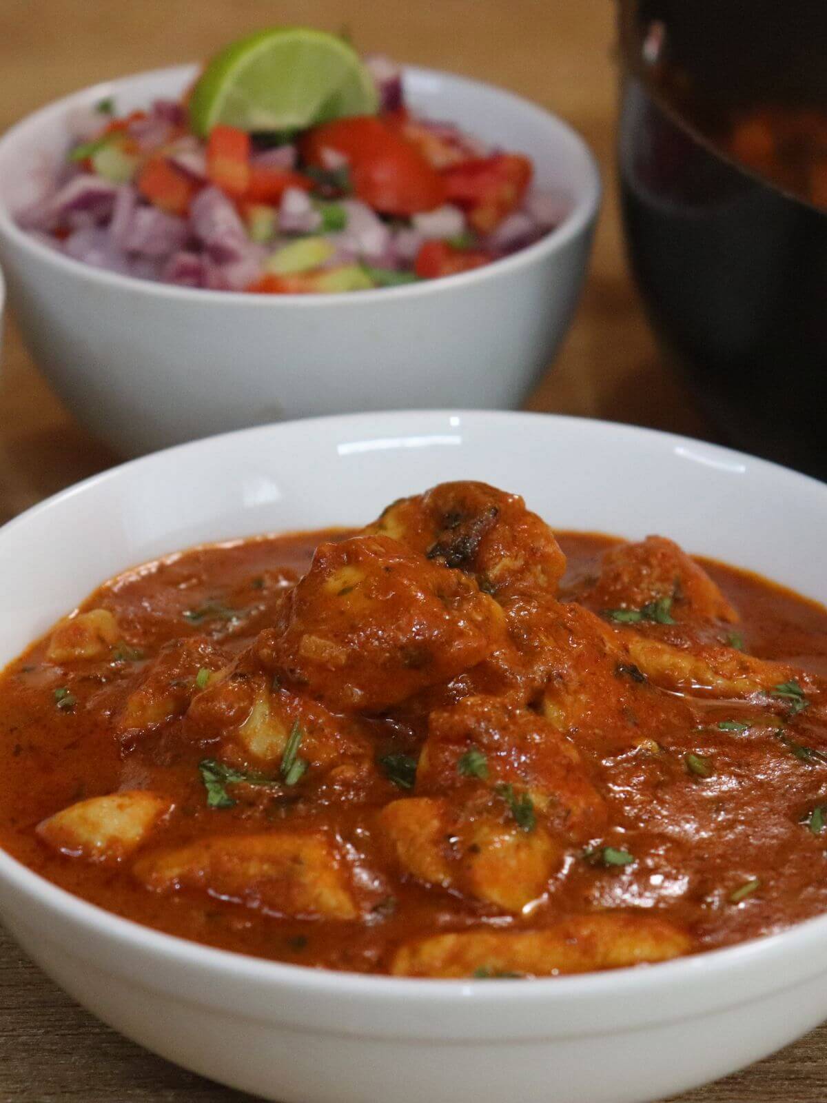 a close-up of chicken chasni served in a bowl. It is served salad in another small bowl and a pot with more chicken chasni curry.