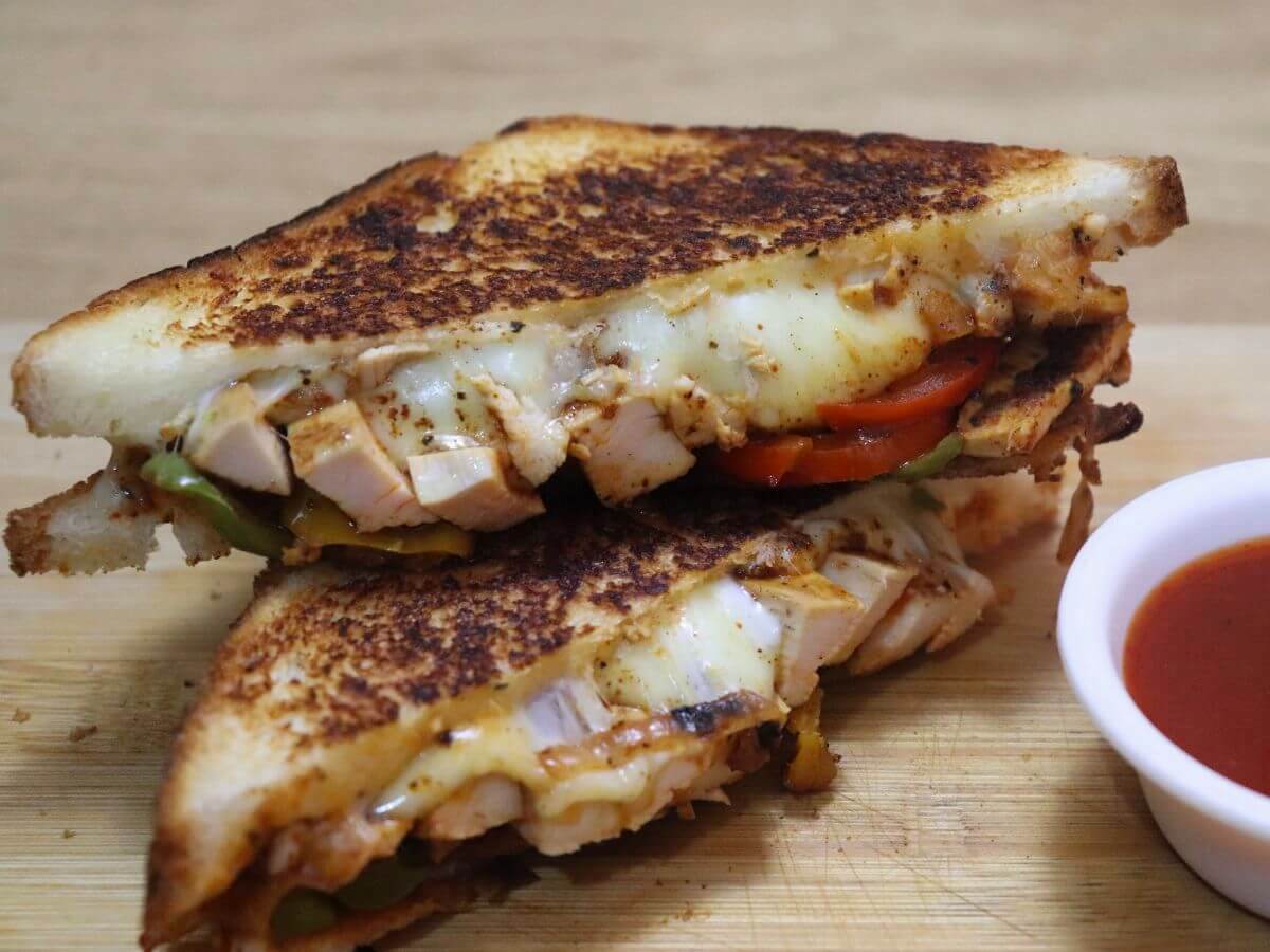 Image of chicken fajita sandwich stacked and placed on a chopping board with a a small bowl of tomato ketchup on the side.