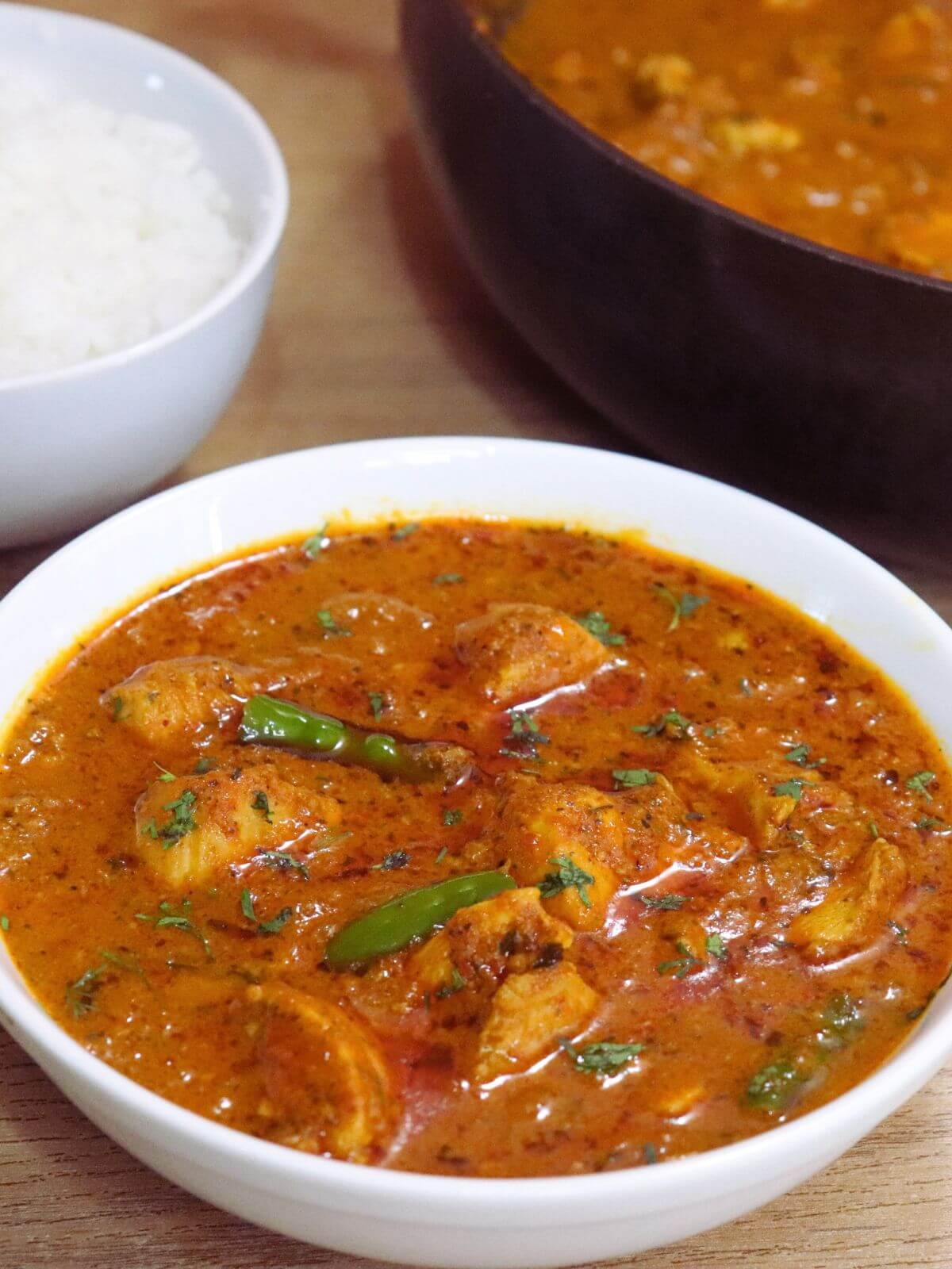 close-up of chicken handi served in a bowl. It is served with rice in another bowl and a pot full of more chicken curry.