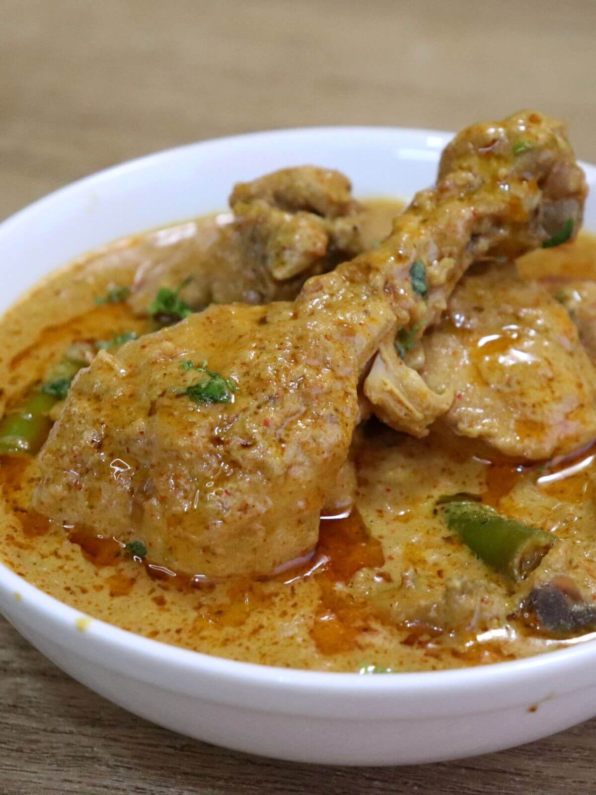 a tight close-up of chicken korma curry served in a white colored bowl.