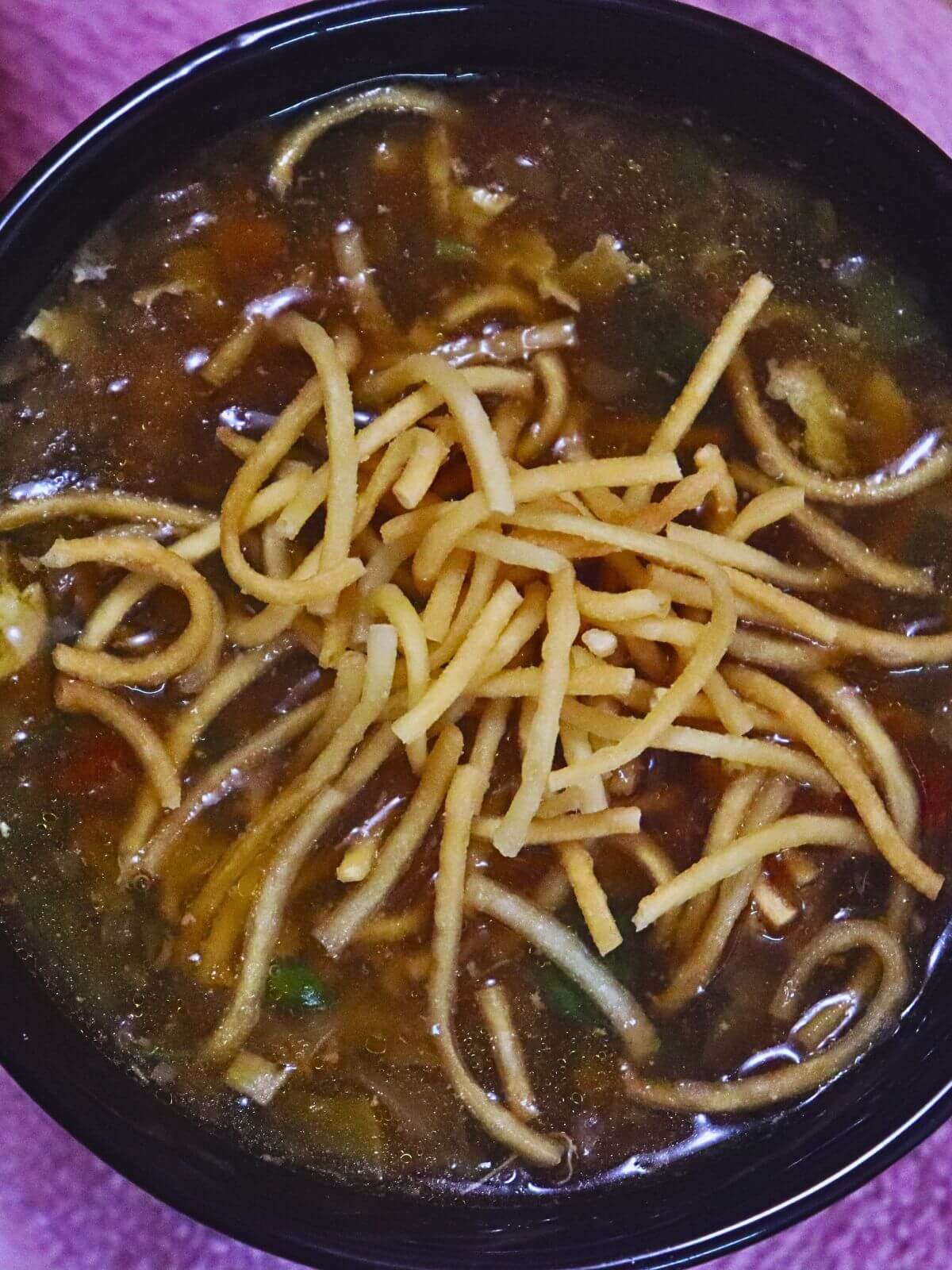 close-up of chicken manchow soup served with fried noodles on the top.