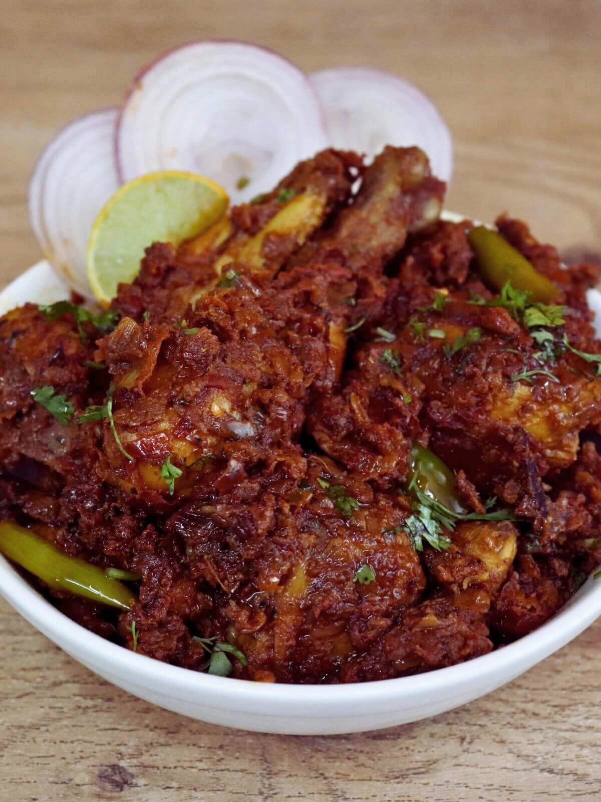chicken masala is served in a white bowl, with onion slices and a lemon wedge on the side.