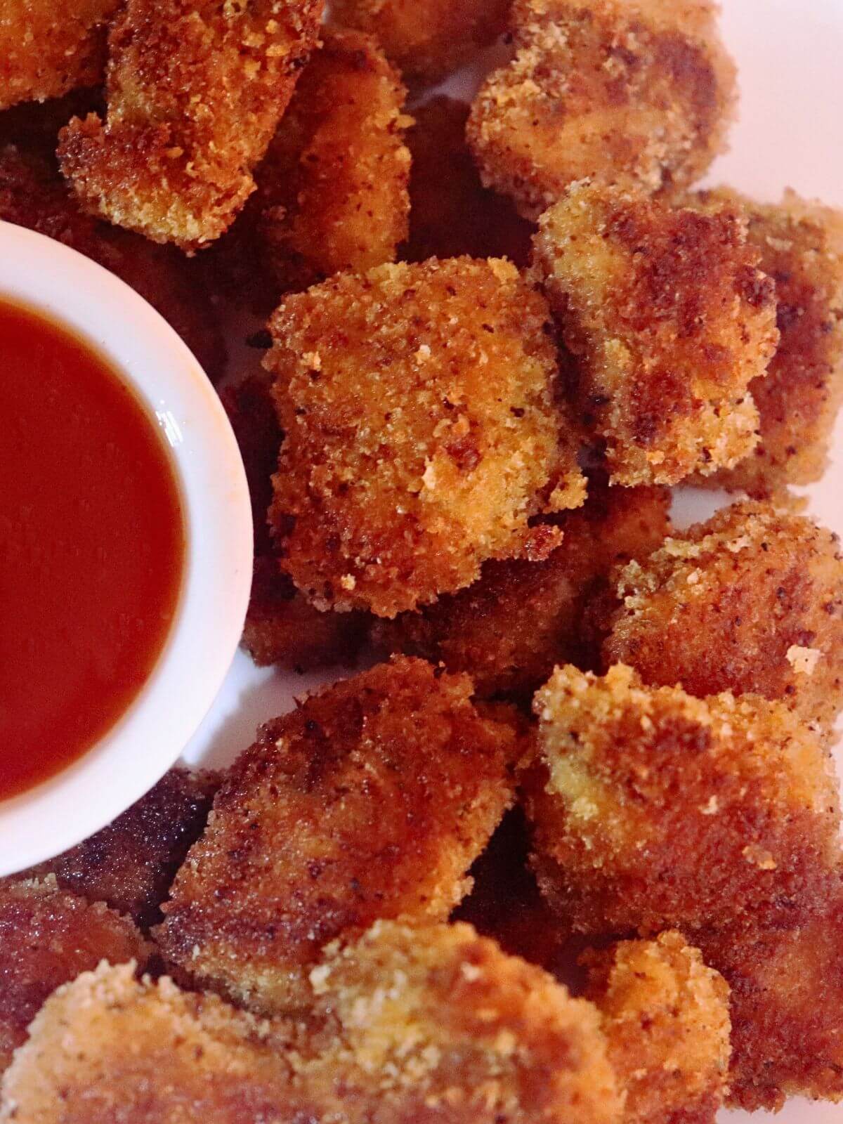 A plate of chicken nuggets is served with a small bowl of tomato ketchup on the side.