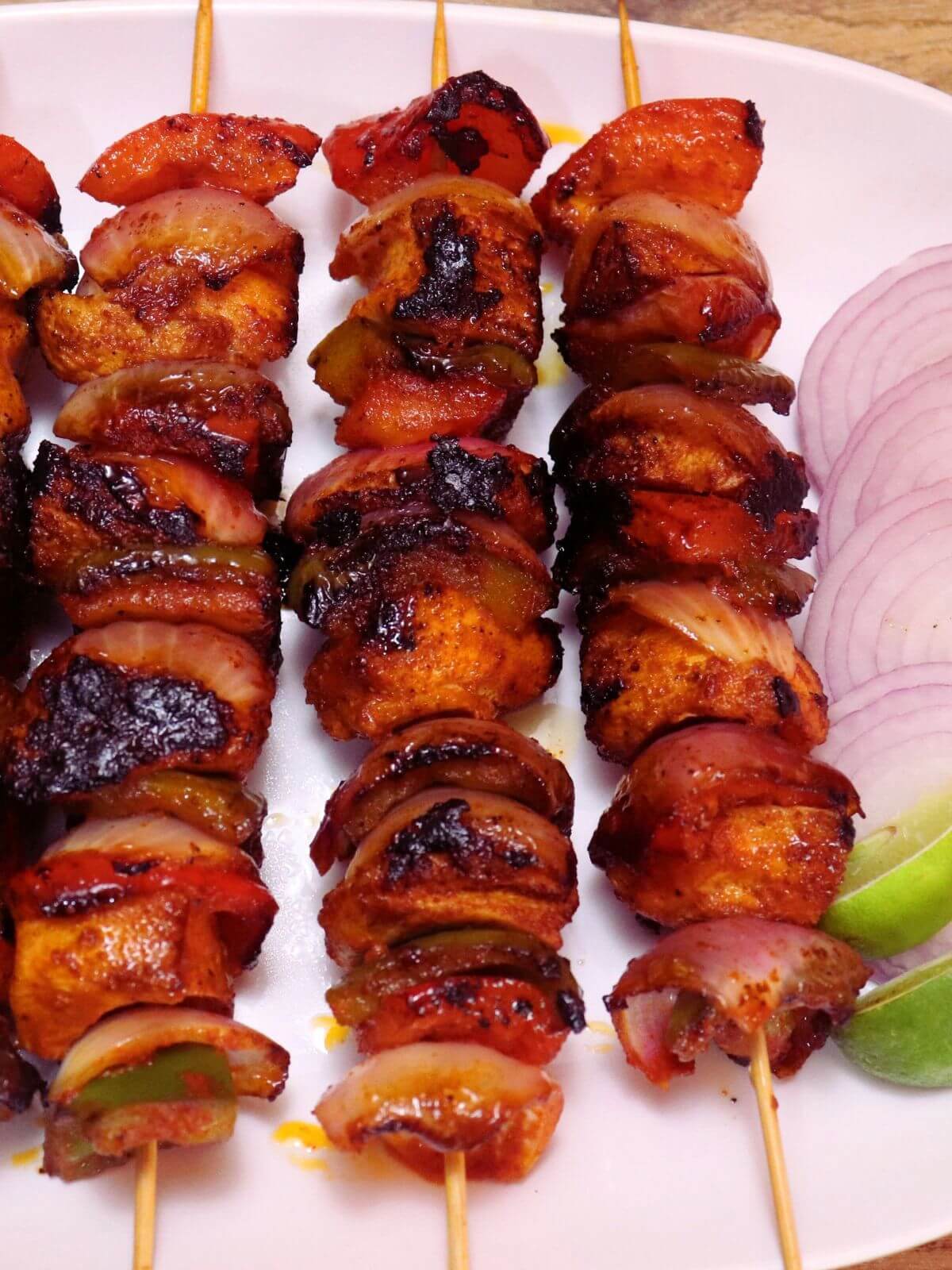 close-up of chicken shashlik. Three chicken shashlik skewers placed on a white plate. It is served with onion slices and lemon wedges.
