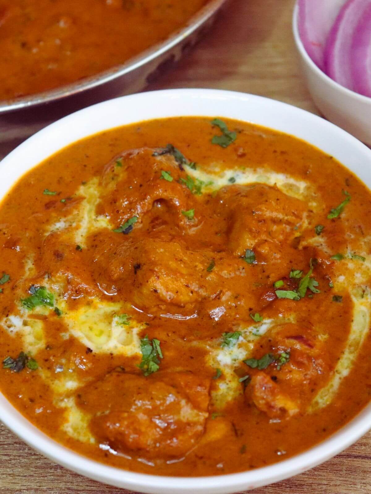A tight close-up of chicken tikka masala served in a bowl, with onion slices served in a small bowl on the side.