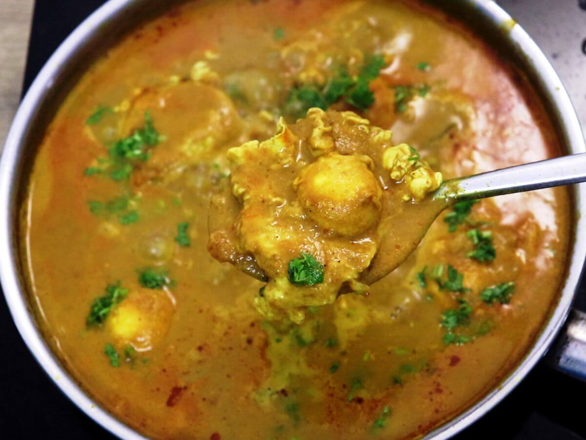 A ladle full of Mangalorean egg drop curry held over the pan.