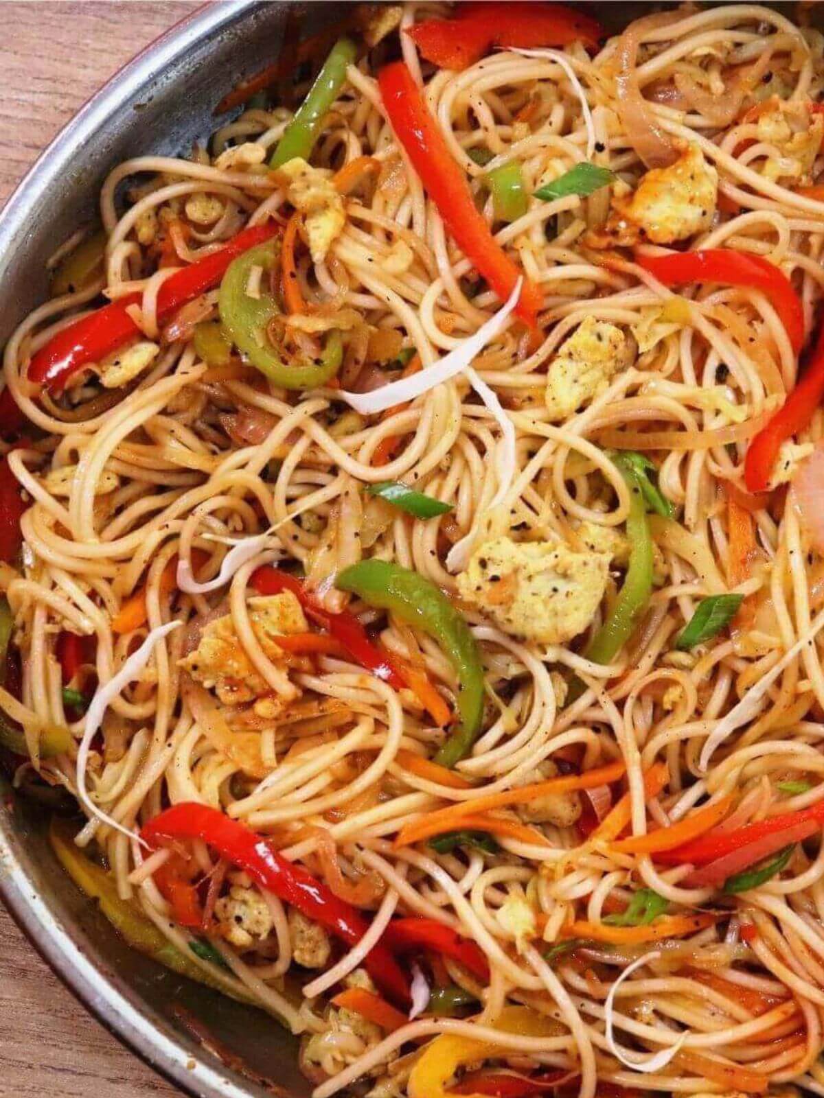A tight close-up of egg hakka noodles in a skillet, with only half the skillet visible in the image.