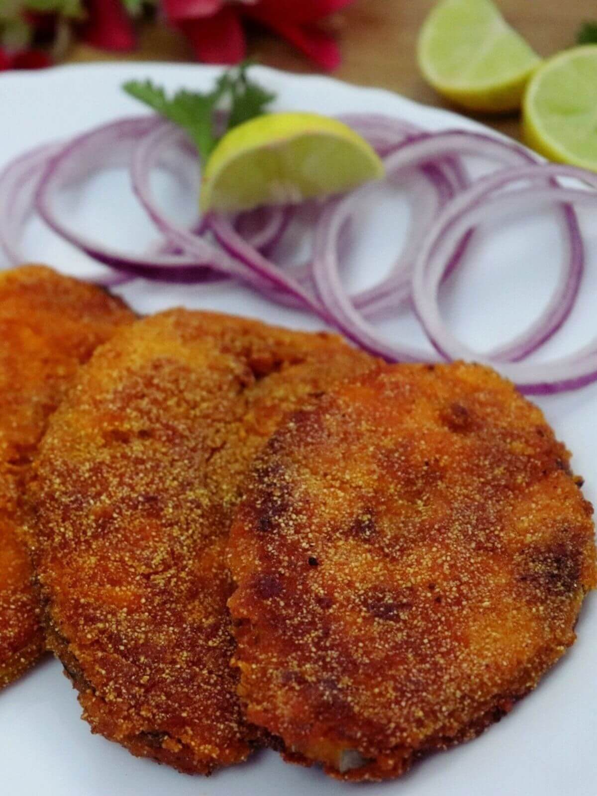 close-up of kingfish fry served on a white plate with onion rings and a lemon wedge.