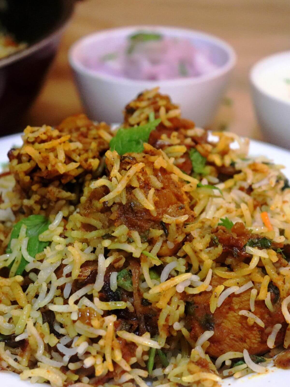 close-up of hyderabadi chicken dum biryani. It is served with salad and raita on the side in another bowl.