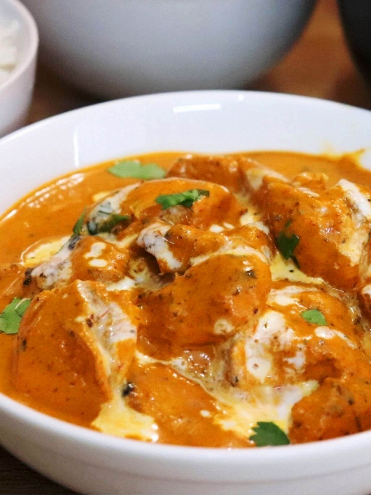 close-up of butter chicken served in a white bowl.