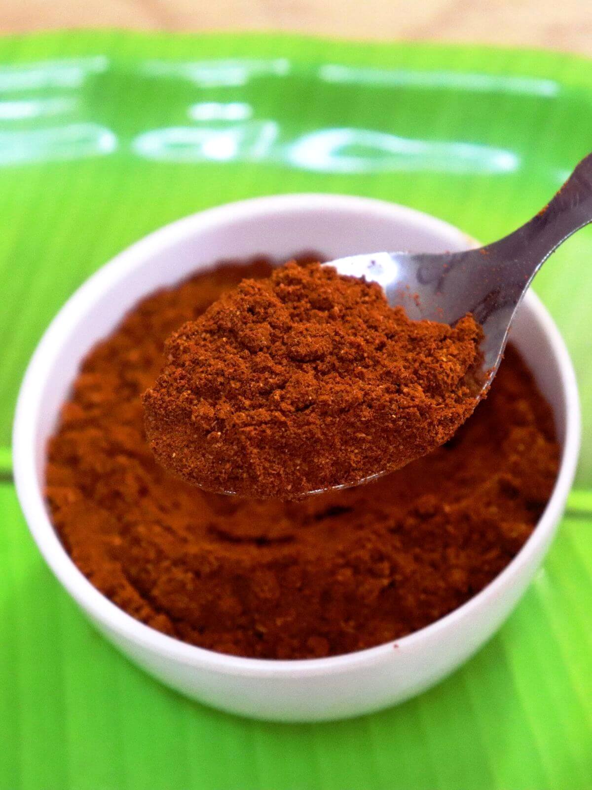 A close-up of Madras curry powder, with a spoonful held over a bowl.