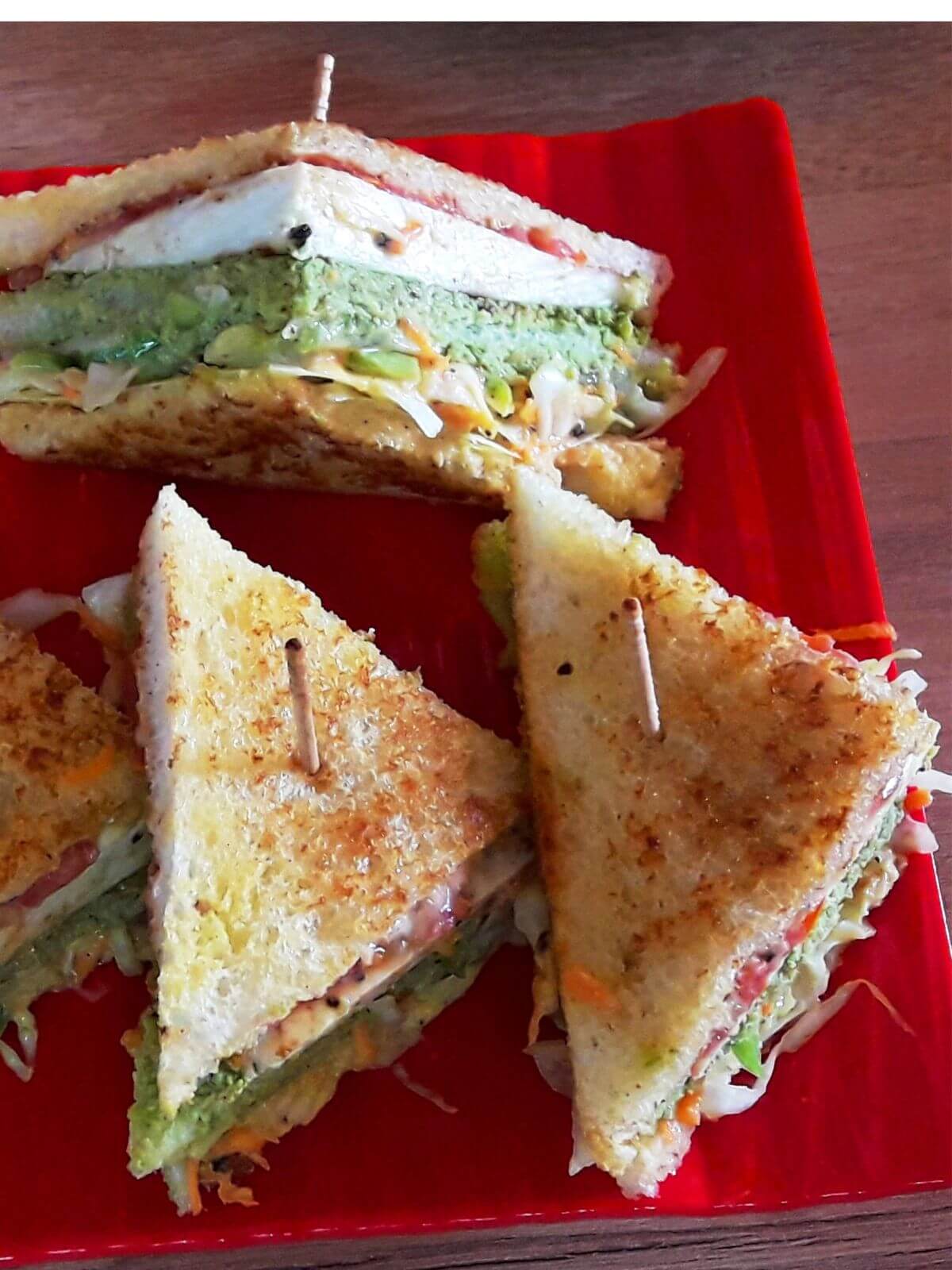 close-up of 3 vegetable club sandwich served on a red color plate.