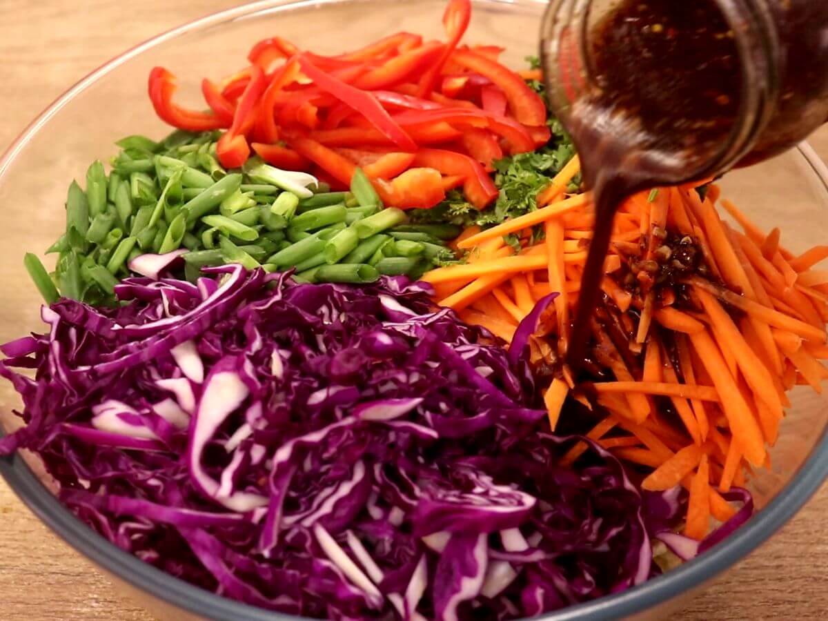 pouring asian slaw dressing over the vegeables.