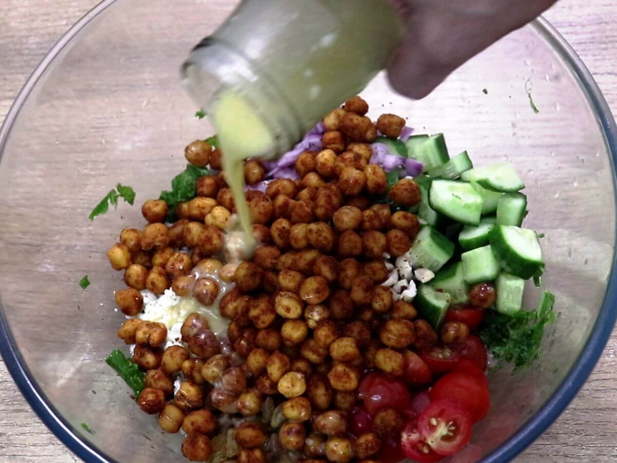 pouring lemon vinaigrette dressing over kale and chickpea salad.