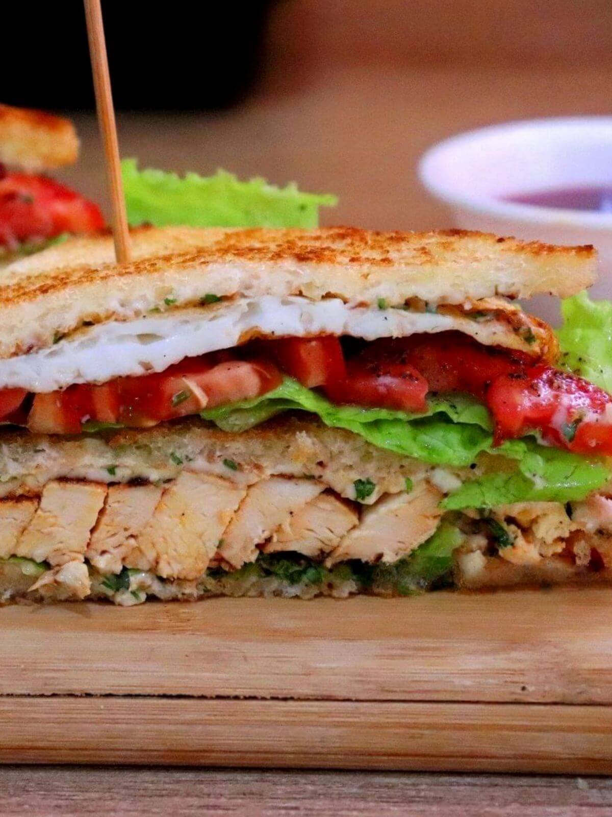 Close-up of a chicken club sandwich, cut in half on a chopping board, revealing all the layers.