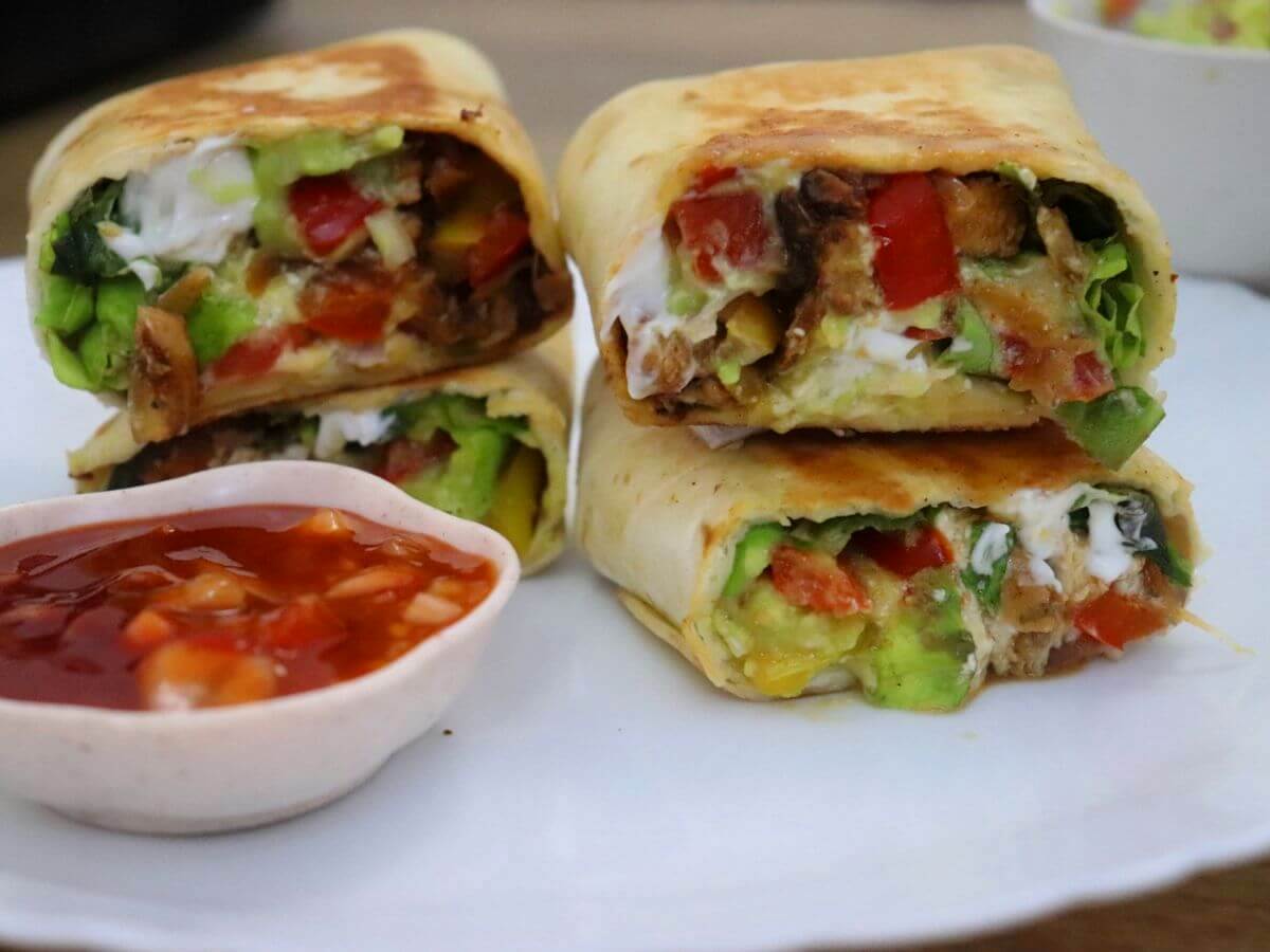close-up of chicken fajita wrap served in a plate with hot sauce on side.
