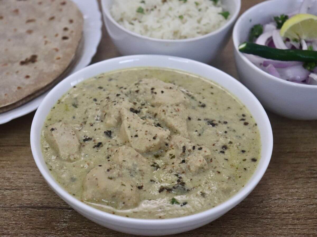 close-up of chicken kali mich served in a bowl. It is served with roti, jeera rice and a bowl of salad on the side.