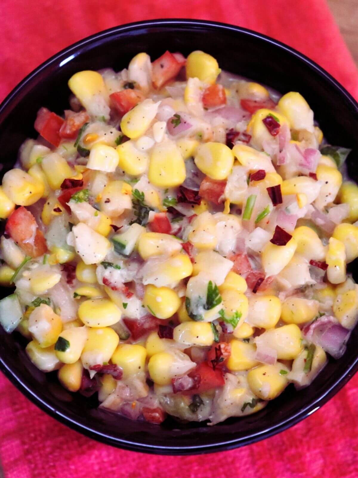 close-up of creamy corn salad in a black color bowl.