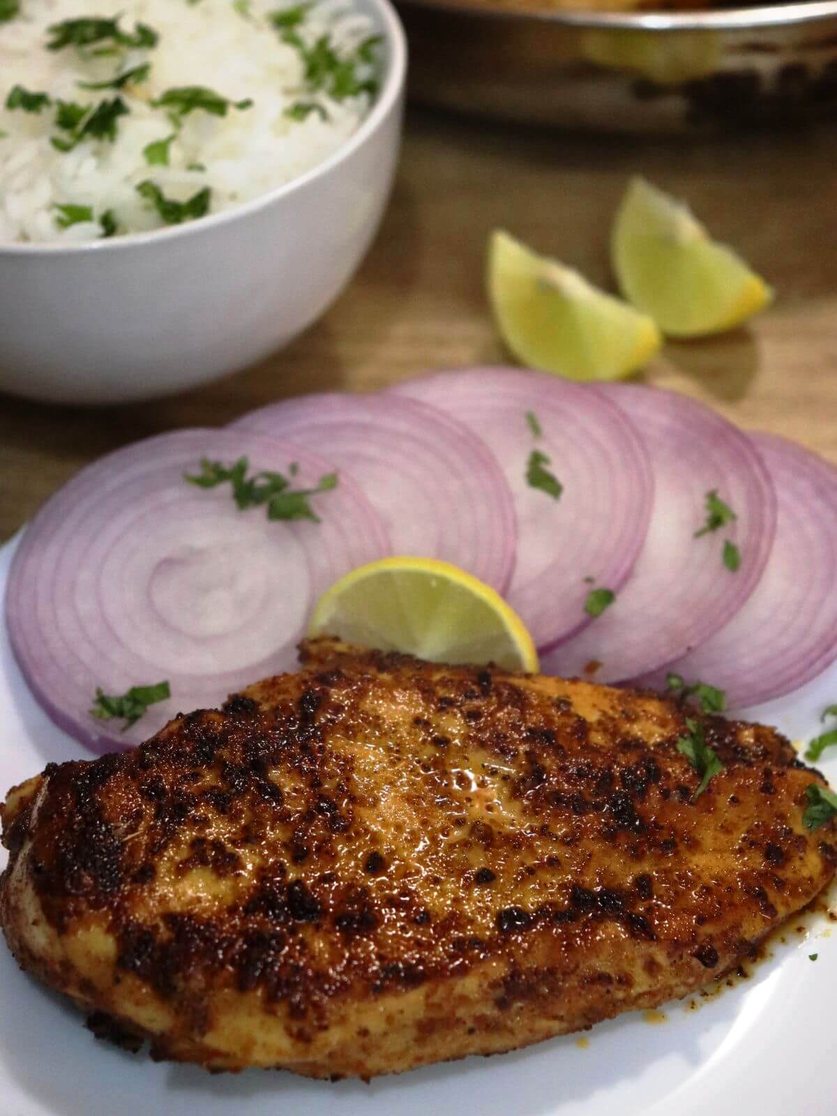 close-up of cumin chicken served in a plate with onion slices and a lemon wedge.