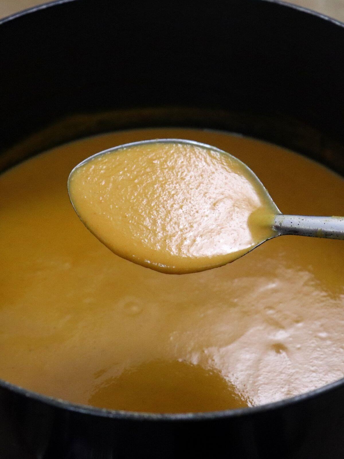 A close-up of curry base gravy is shown, with a ladle, positioned over a pot and full of the curry base.