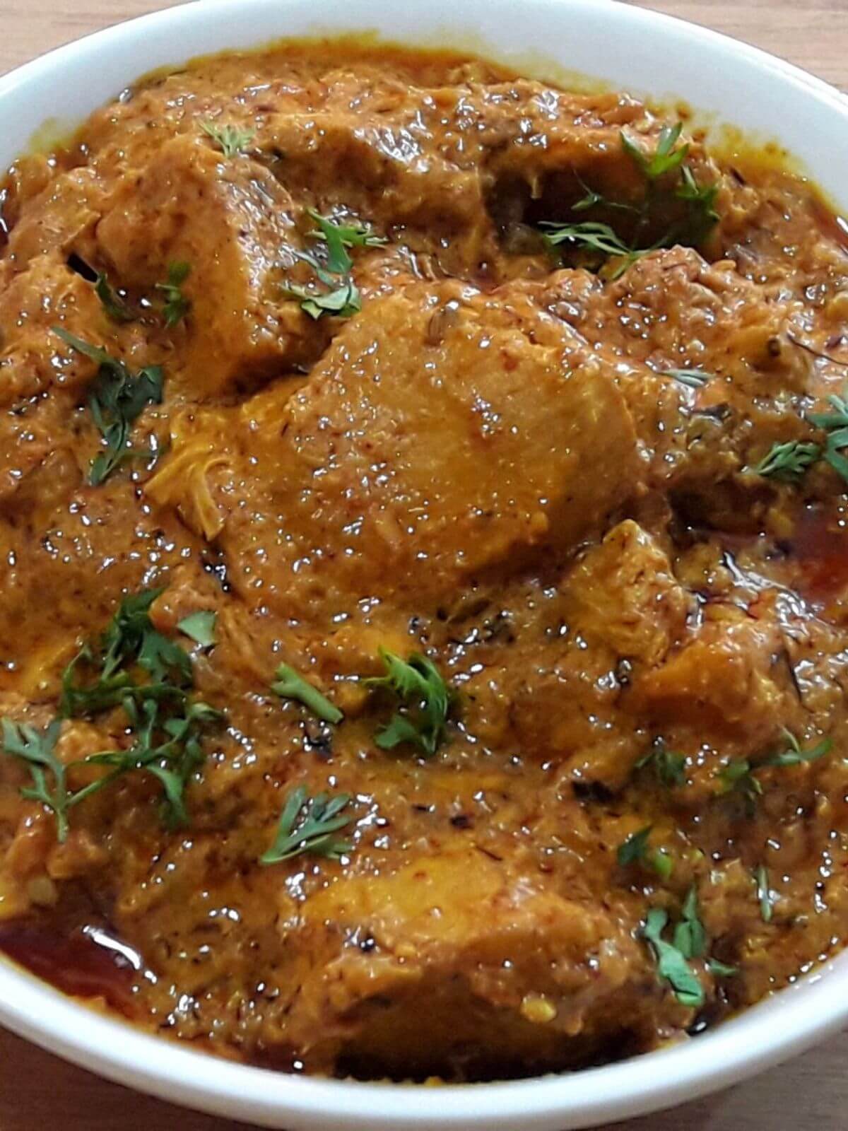 close-up of dahi chicken served in a white bowl.
